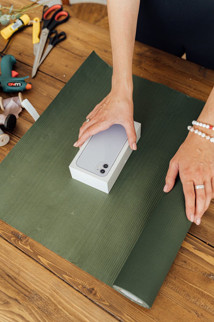 Hands wrapping a smartphone in green paper, perfect for gifting or special occasions.