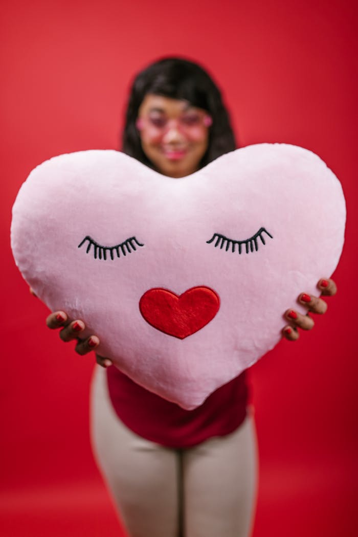 A person holding a heart-shaped pillow with a red heart design, ideal for Valentine’s Day gift ideas.